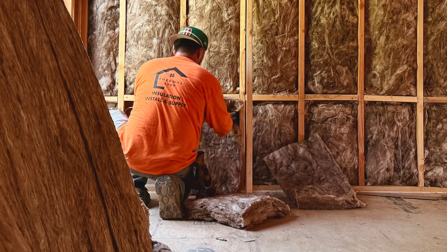 Thermal Shop installer kneeling to fit fiberglass batts between wall studs