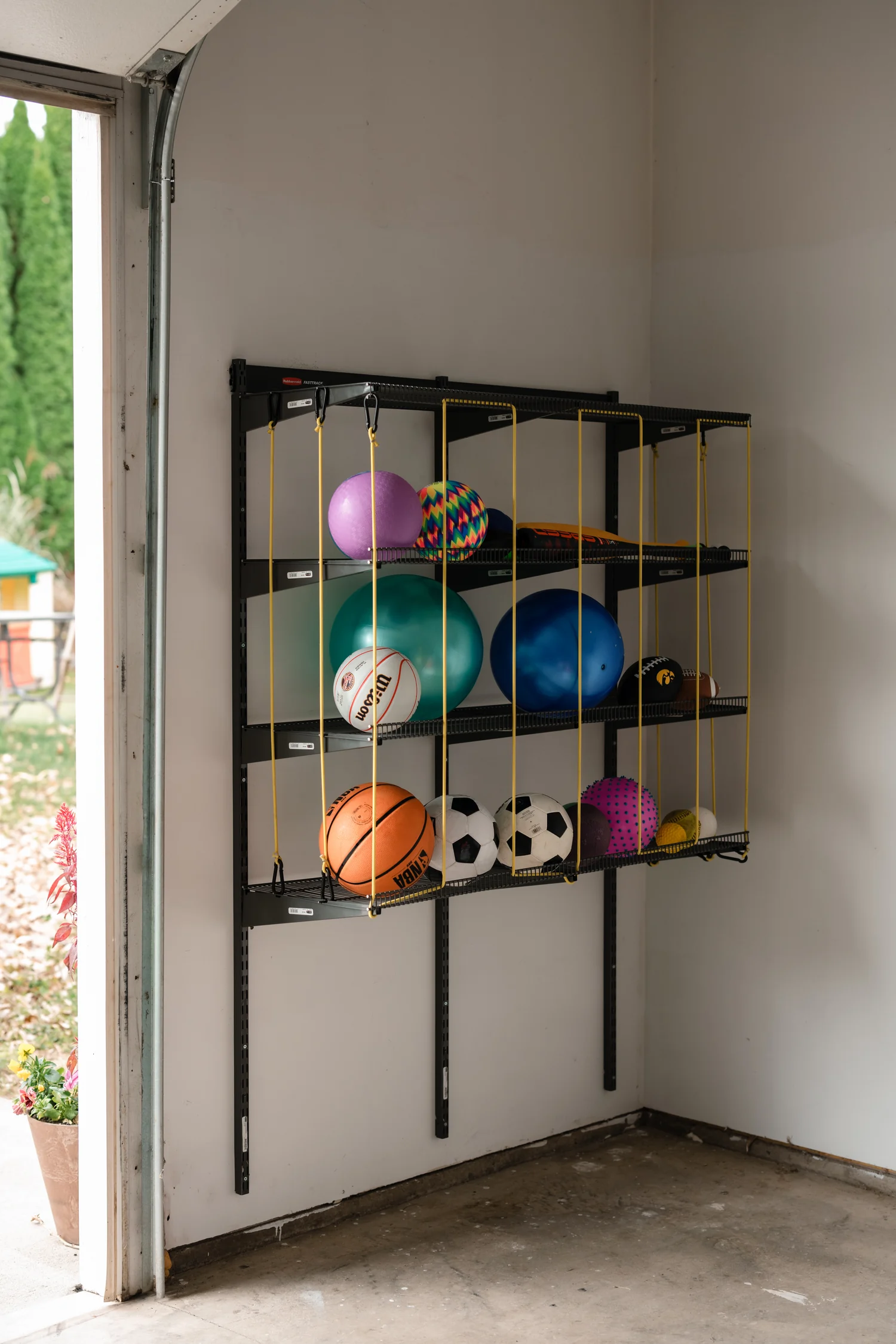Gray garage shelving with yellow bungee cords holding sports balls on a garage wall
