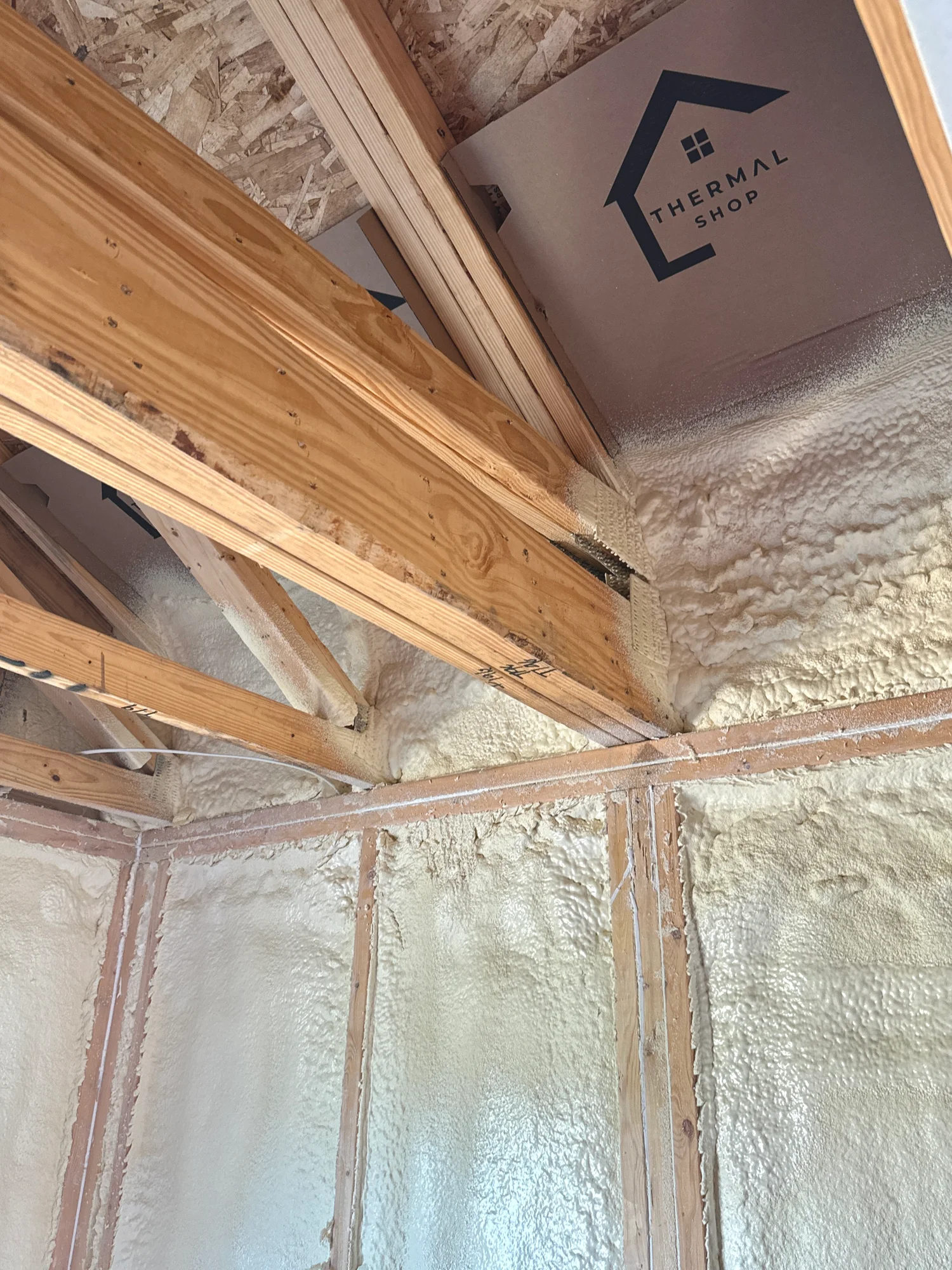 Fresh spray foam sealing the joint where rafters meet the top plate, with a Thermal Shop box against the roof deck